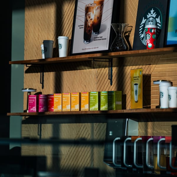 Starbucks coffee and Teavana tea products are displayed on wooden shelves against a textured wall.