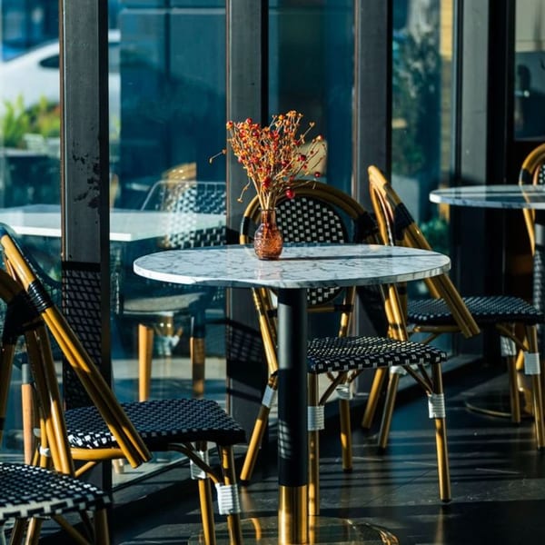 Olia Restaurant's outdoor seating area with marble tables, wicker chairs, and a small vase of flowers.