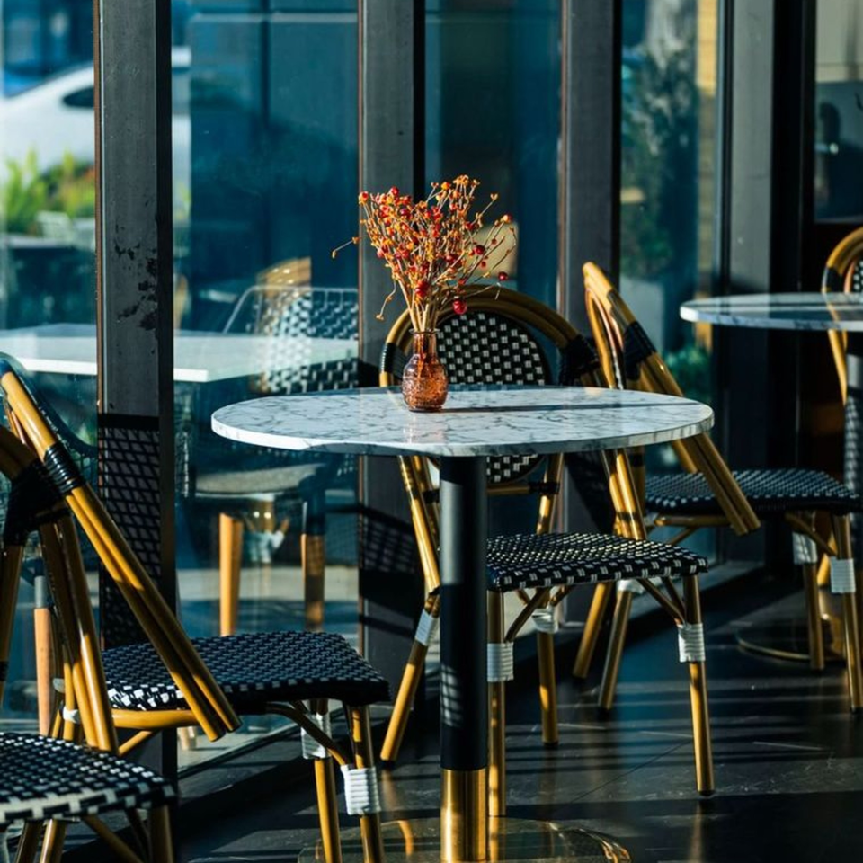 Olia Restaurant's outdoor seating area with marble tables, wicker chairs, and a small vase of flowers.