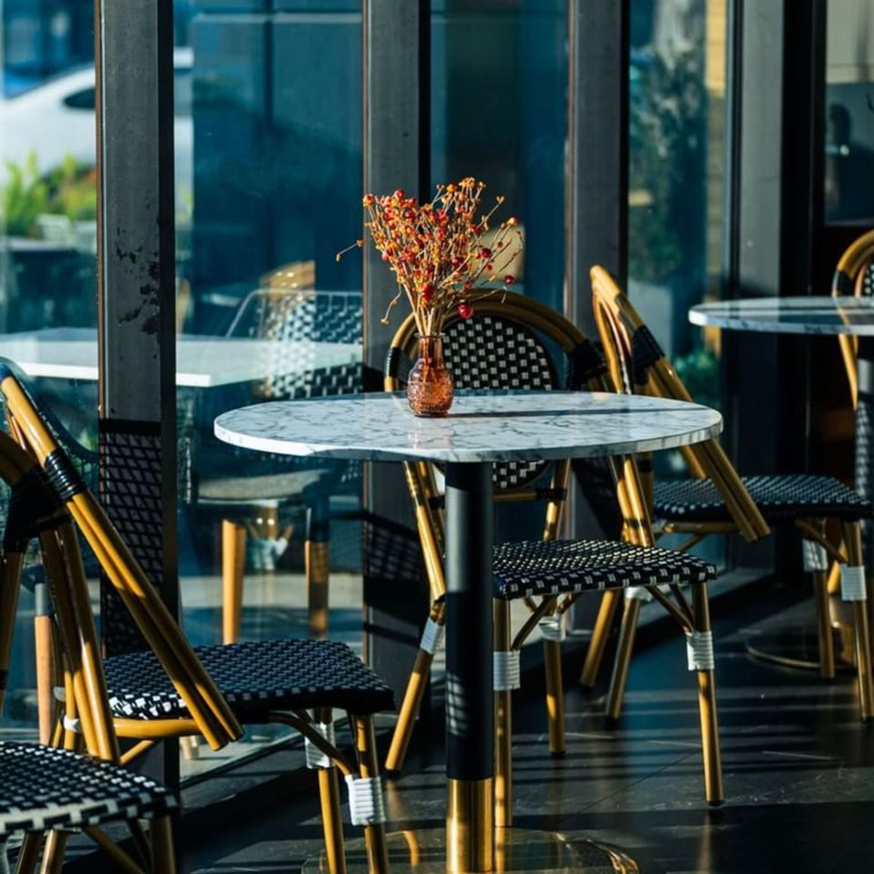 Olia Restaurant's outdoor seating area with marble tables, wicker chairs, and a small vase of flowers.