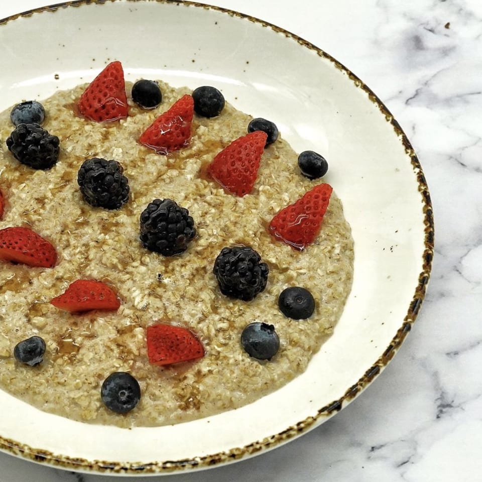 Olia Restaurant's oatmeal topped with fresh strawberries, blueberries, and blackberries, drizzled with honey.