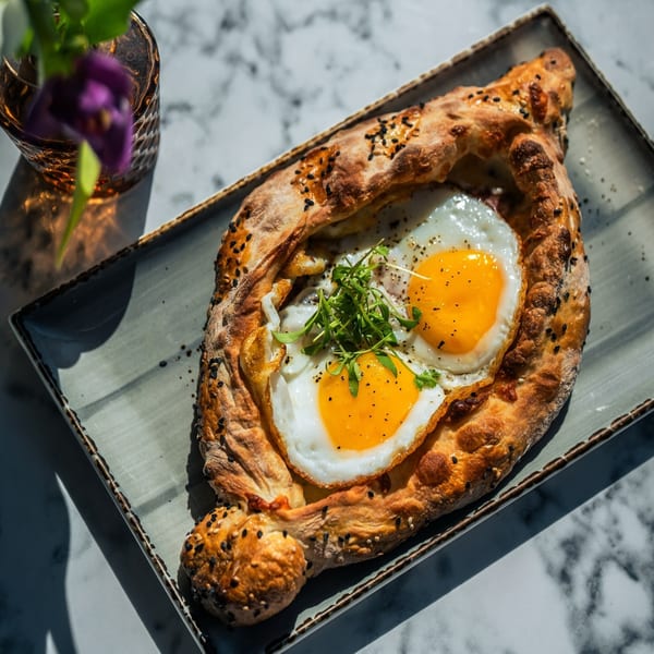 Olia Restaurant's Mediterranean khachapuri with two fried eggs, fresh greens, and black sesame seeds.