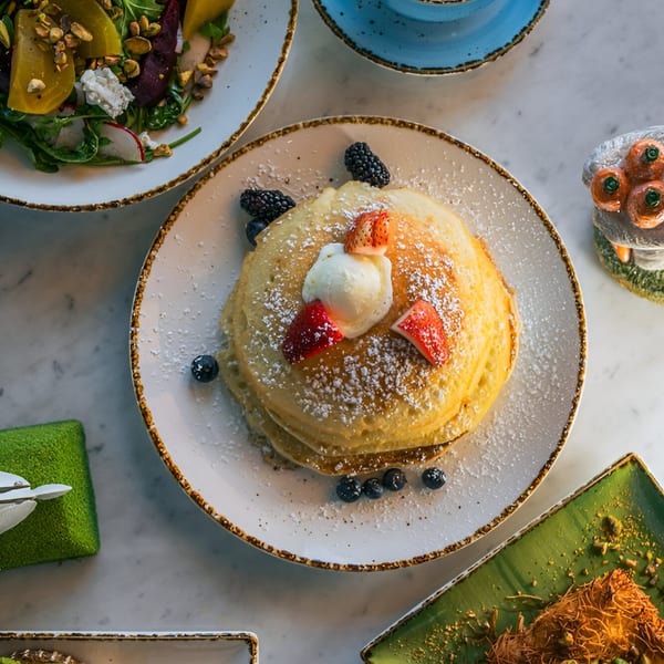 A stack of pancakes with berries, whipped cream, and powdered sugar, alongside a salad.