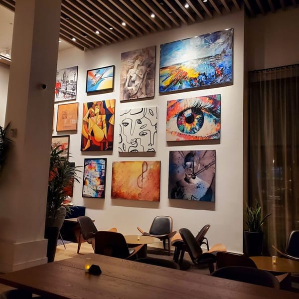 A wall in Olia Restaurant adorned with various colorful abstract paintings, with modern seating below.