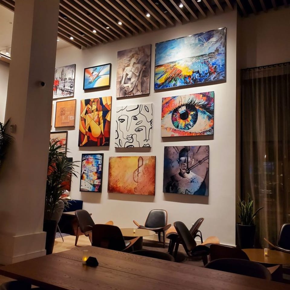 A wall in Olia Restaurant adorned with various colorful abstract paintings, with modern seating below.