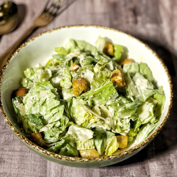 A fresh Caesar salad with crisp romaine lettuce, croutons, and creamy dressing in a light green bowl.