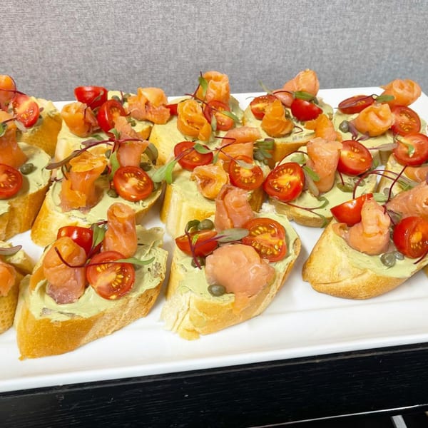 Platter of Mediterranean bruschetta topped with salmon, cherry tomatoes, capers, and microgreens.