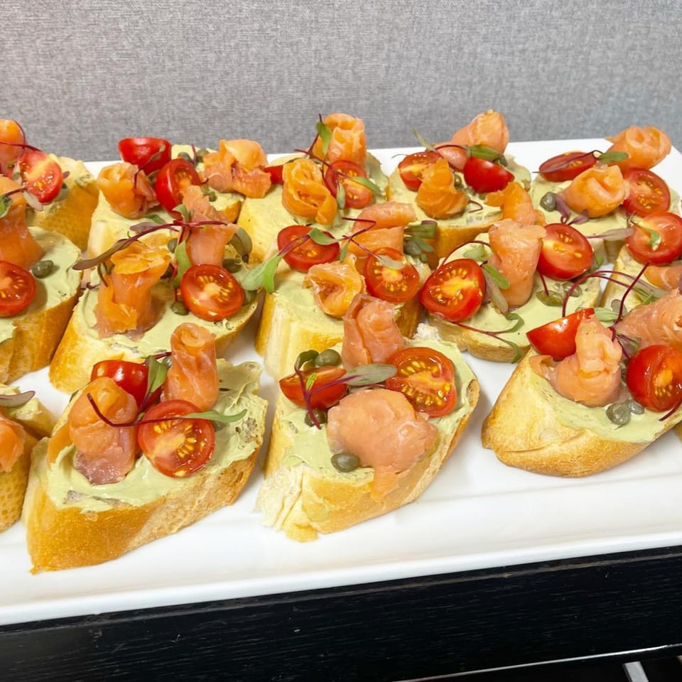Platter of Mediterranean bruschetta topped with salmon, cherry tomatoes, capers, and microgreens.