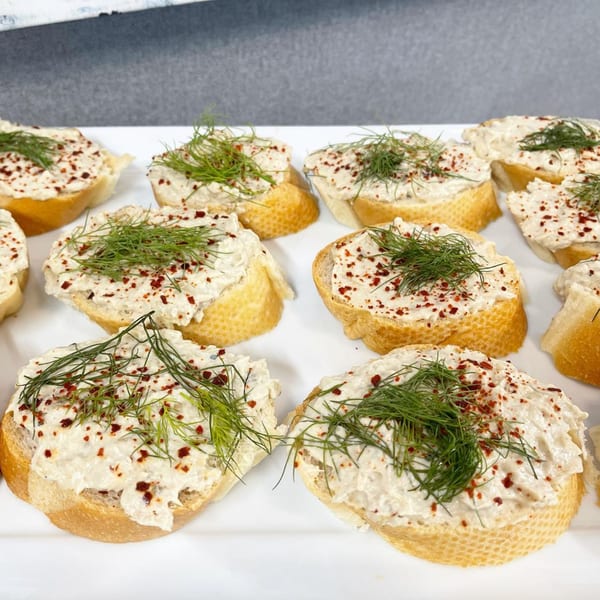 A white platter filled with Mediterranean crostini, topped with a creamy spread, dill, and red pepper flakes.